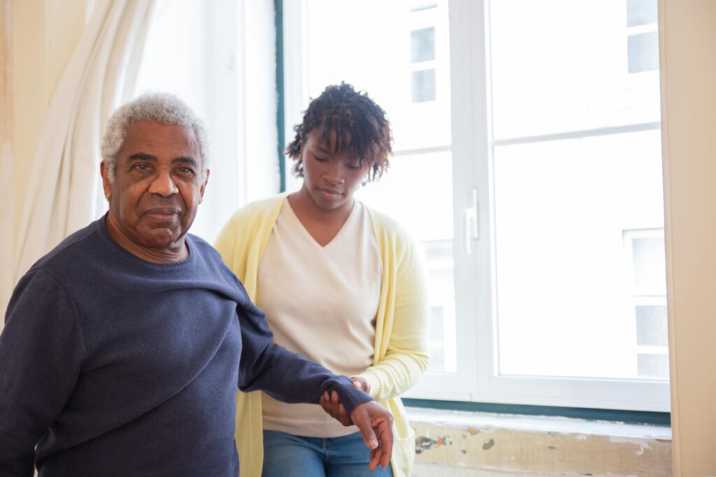 An elderly man receives care from a young woman near a bright window in Portugal.